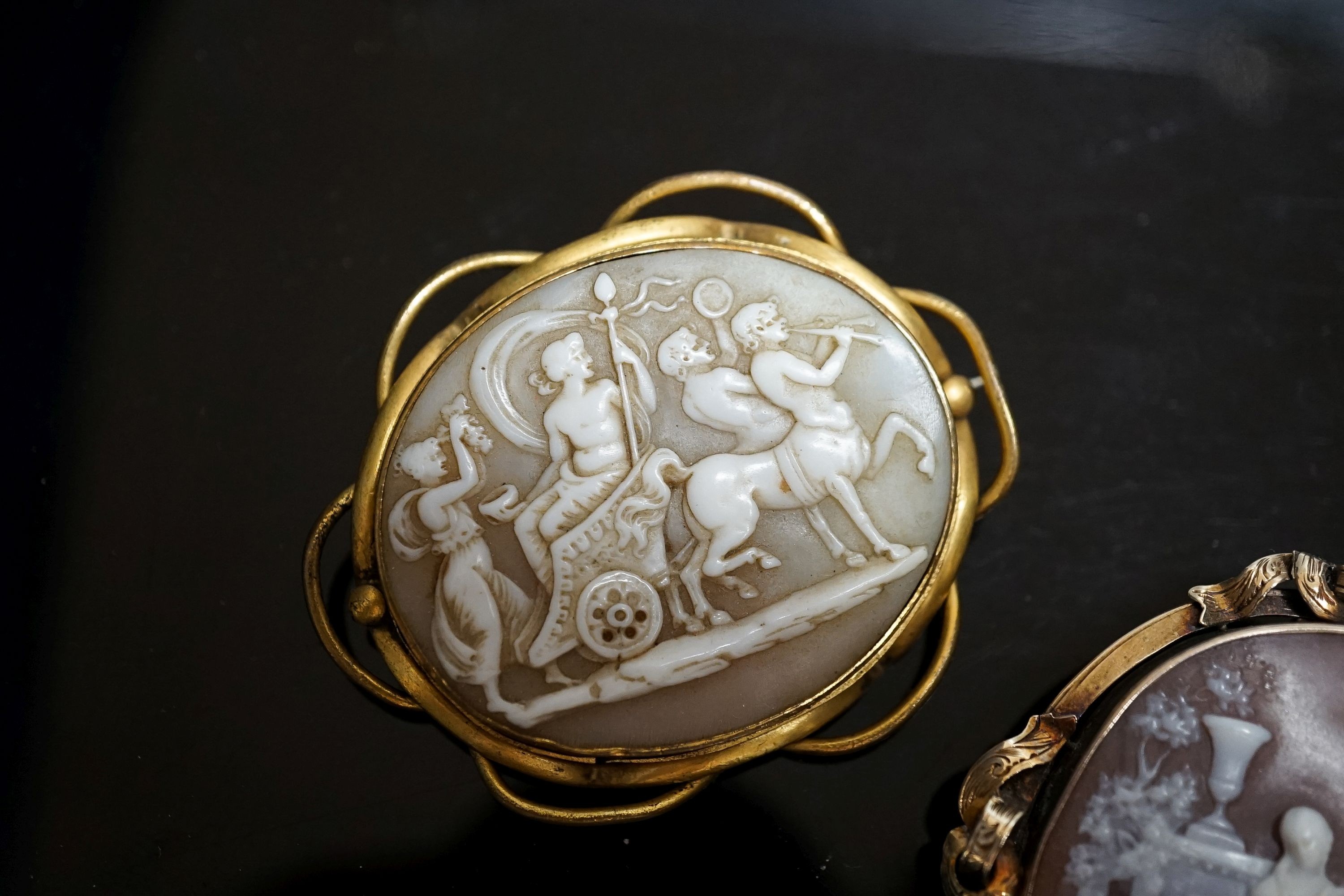 An Edwardian yellow metal mounted carved oval cameo shell and a gilt metal mounted cameo shell carved with chariot and mythical creatures, 52mm.